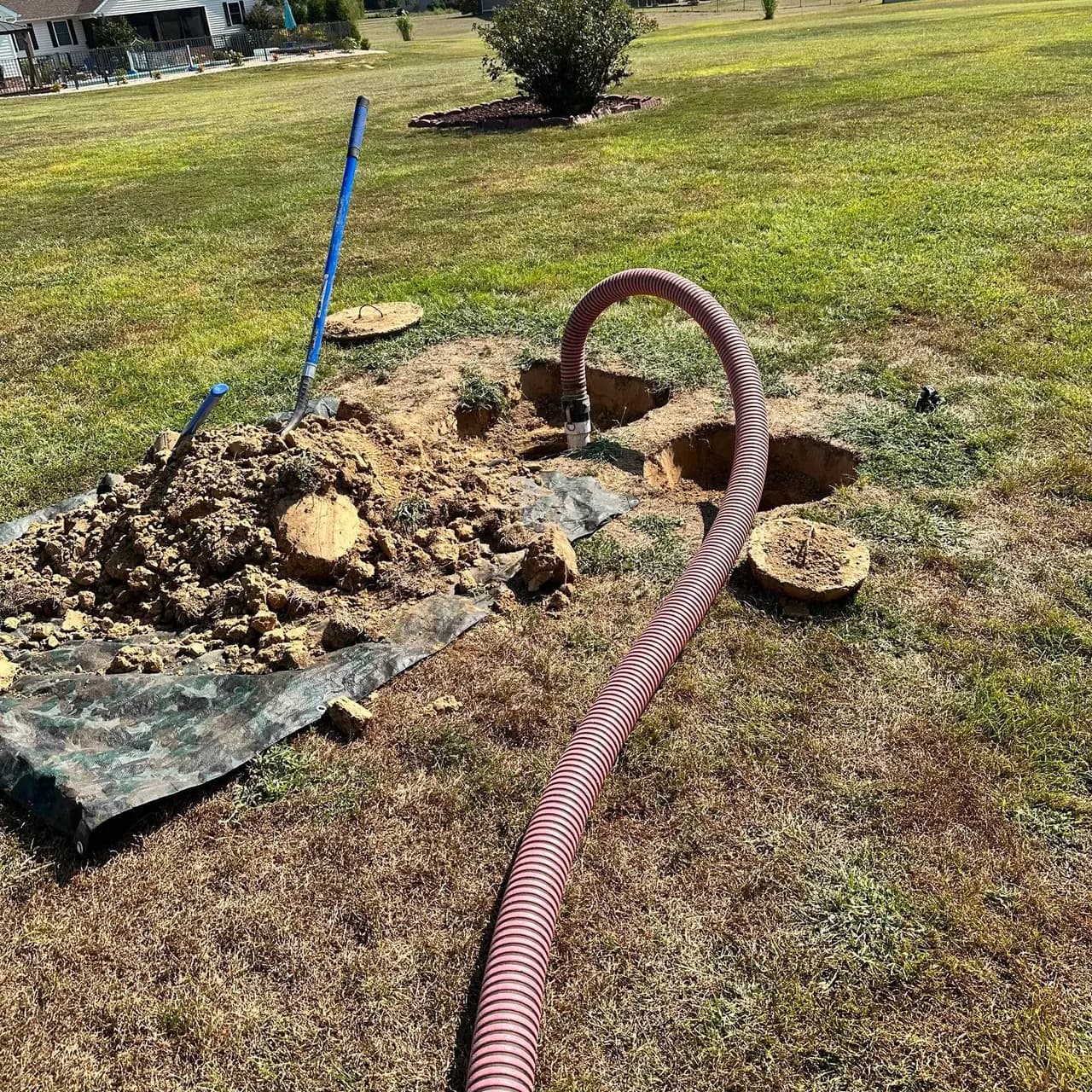 Septic tank lids dug out and uncovered in a lawn, with a pump hose ready